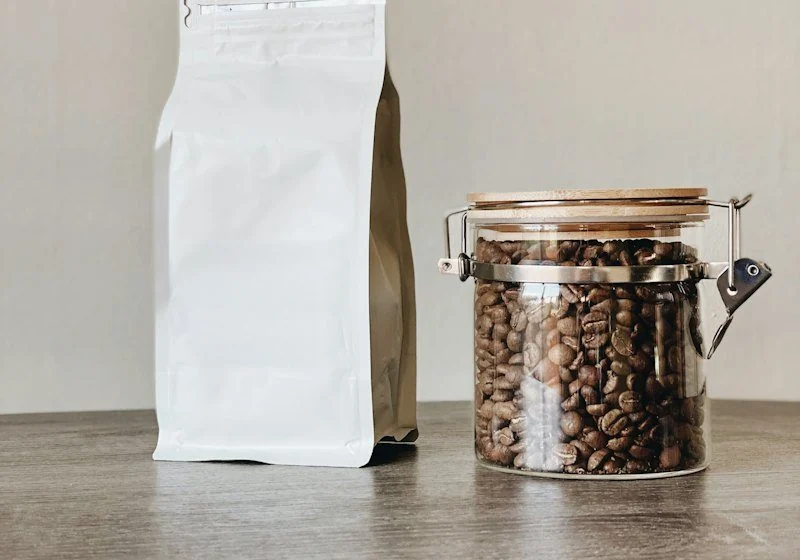 A plain white coffee bag beside a jar of roasted beans